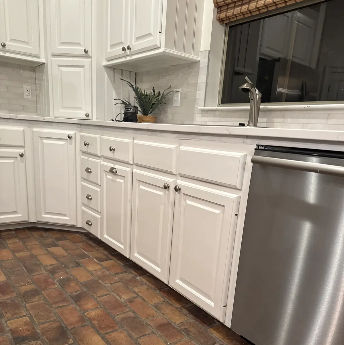 Kitchen with raised-panel cabinets refinished in white, over a brick paver floor.