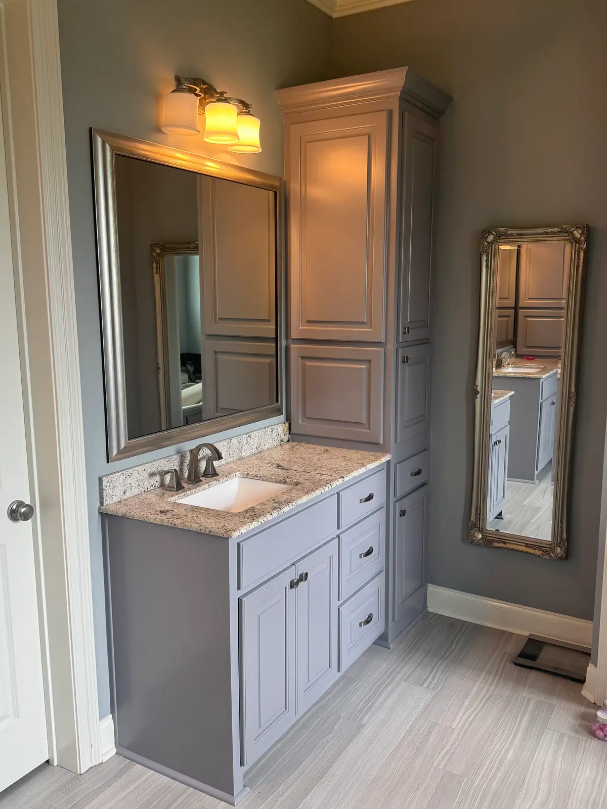 Bathroom vanity and full-height linen cabinet painted soft grey against warm grey walls.
